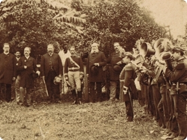 Detalle de fotograf&iacute;a: Acto al aire libre en el marco de la devoluci&oacute;n al Paraguay de los trofeos obtenidos en la Guerra de la Triple Alianza, por parte de la Comisi&oacute;n Oriental en 1885. Banda militar ejecuta sus instrumentos y delegaciones. Ca. 1885.